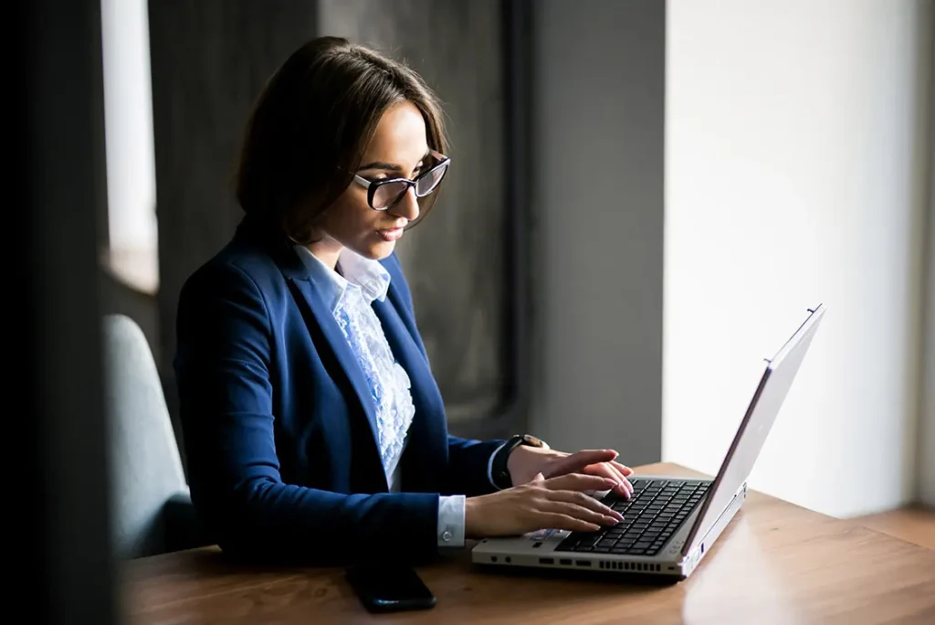 Mulher de óculos e terno azul digitando em um laptop